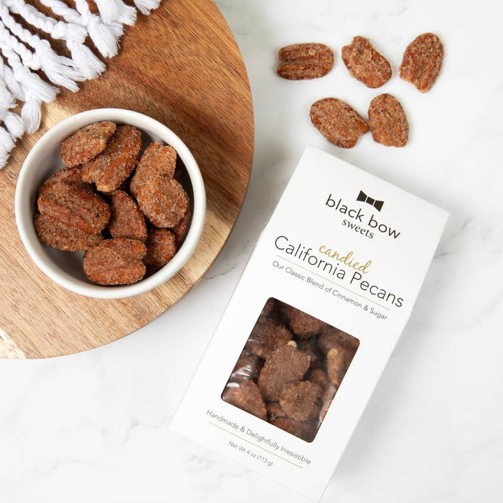 Elegant black and white box of Black Bow Sweets Candied Pecans next to a bowl of candied pecans, perfect for gifting or entertaining.