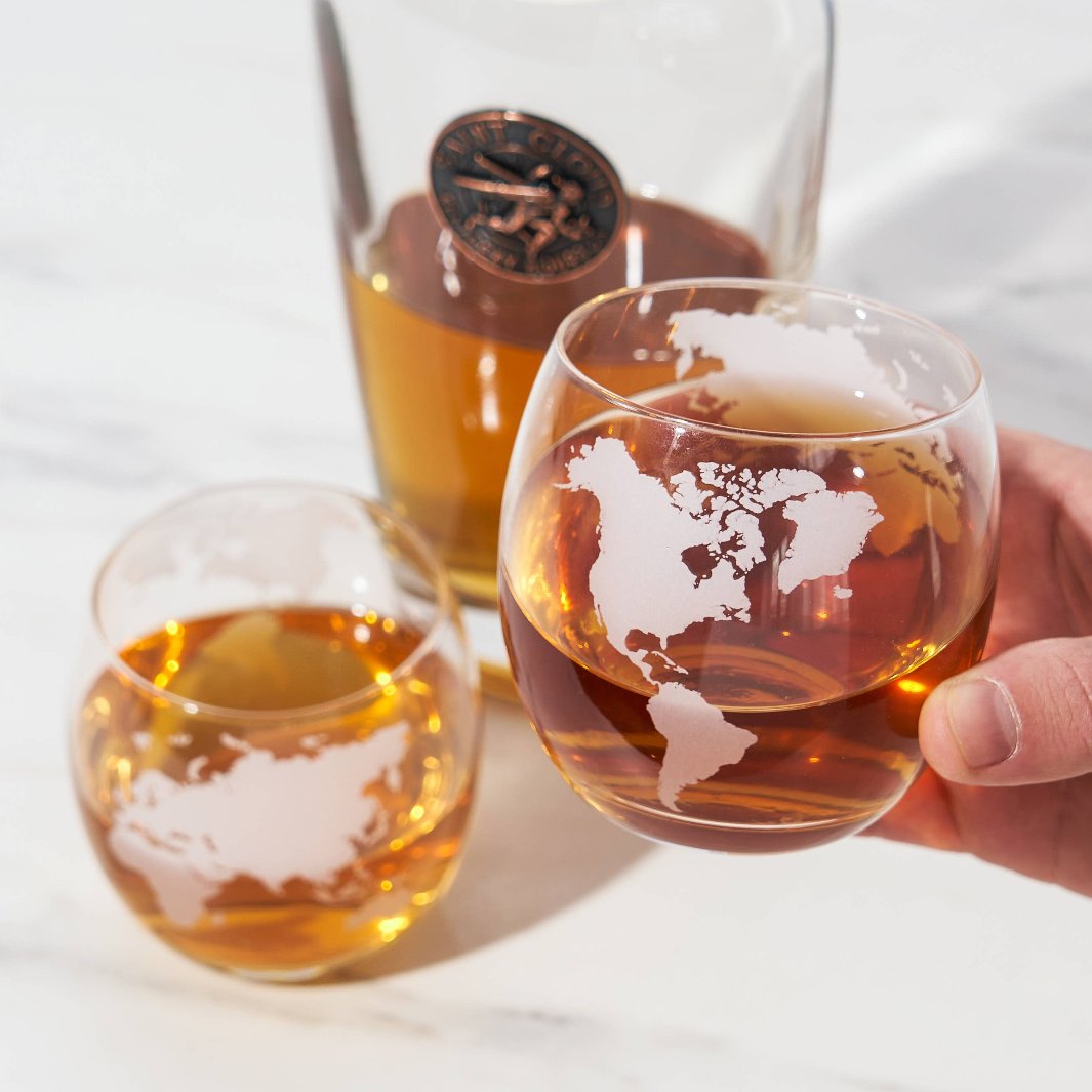 Close-up picture of person holding globe themed whiskey rocks glass. 