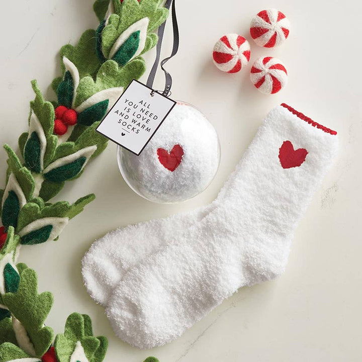 Close-up view of white socks with red heart design, and shown packaged in a clear, festive ornament with a holiday gift tag.