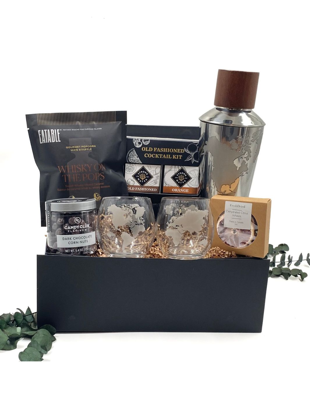 Curated gift box featuring a globe-themed stainless steel cocktail shaker, two globe whiskey tumblers, a set of white marble whiskey stones in a velvet bag, Old Fashioned cocktail kit, dried citrus garnishes, gourmet caramel popcorn, and dark chocolate corn nuts