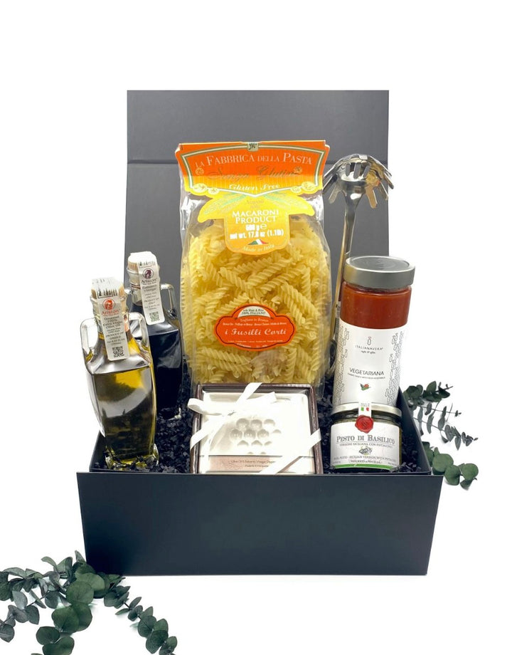 Contents of the Pasta Perfection Gluten Free Gift Box, including gluten-free fusilli pasta, pesto, tomato sauce, EVOO, balsamic vinegar, dipping plate, and pasta serving spoon.